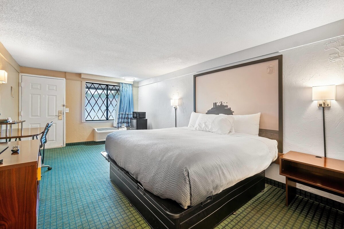 Une chambre d’hôtel avec un grand lit, un bureau, une chaise, une lampe et une fenêtre donnant sur un beau paysage.