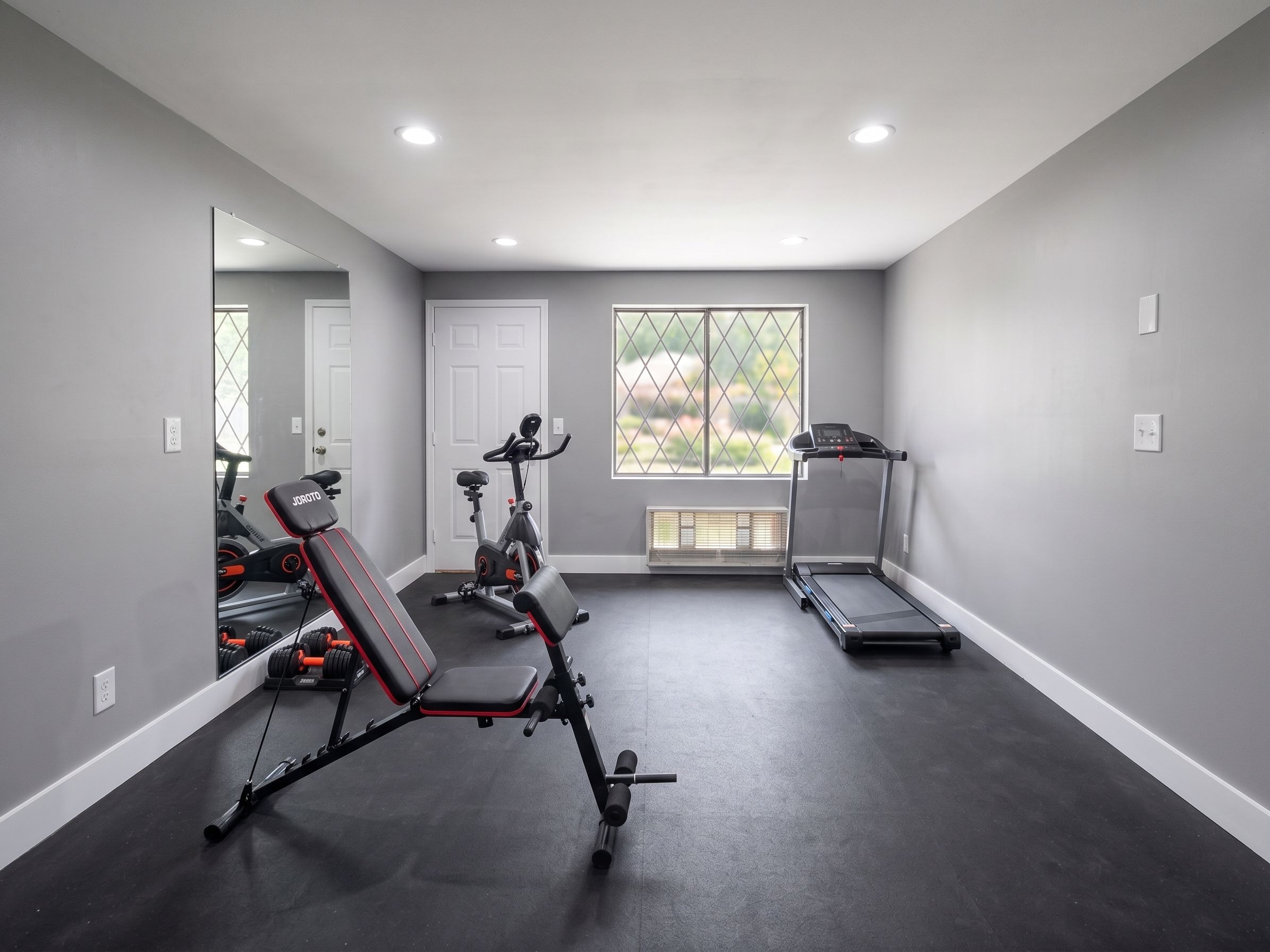 Un gimnasio en casa con equipo de ejercicio, una cinta de correr y un espejo grande.