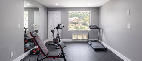 Un gimnasio en casa con equipo de ejercicio, una cinta de correr y un espejo grande.