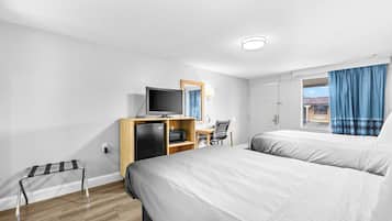 Una habitación de hotel con dos camas, un escritorio con computadora, un televisor y un refrigerador pequeño.