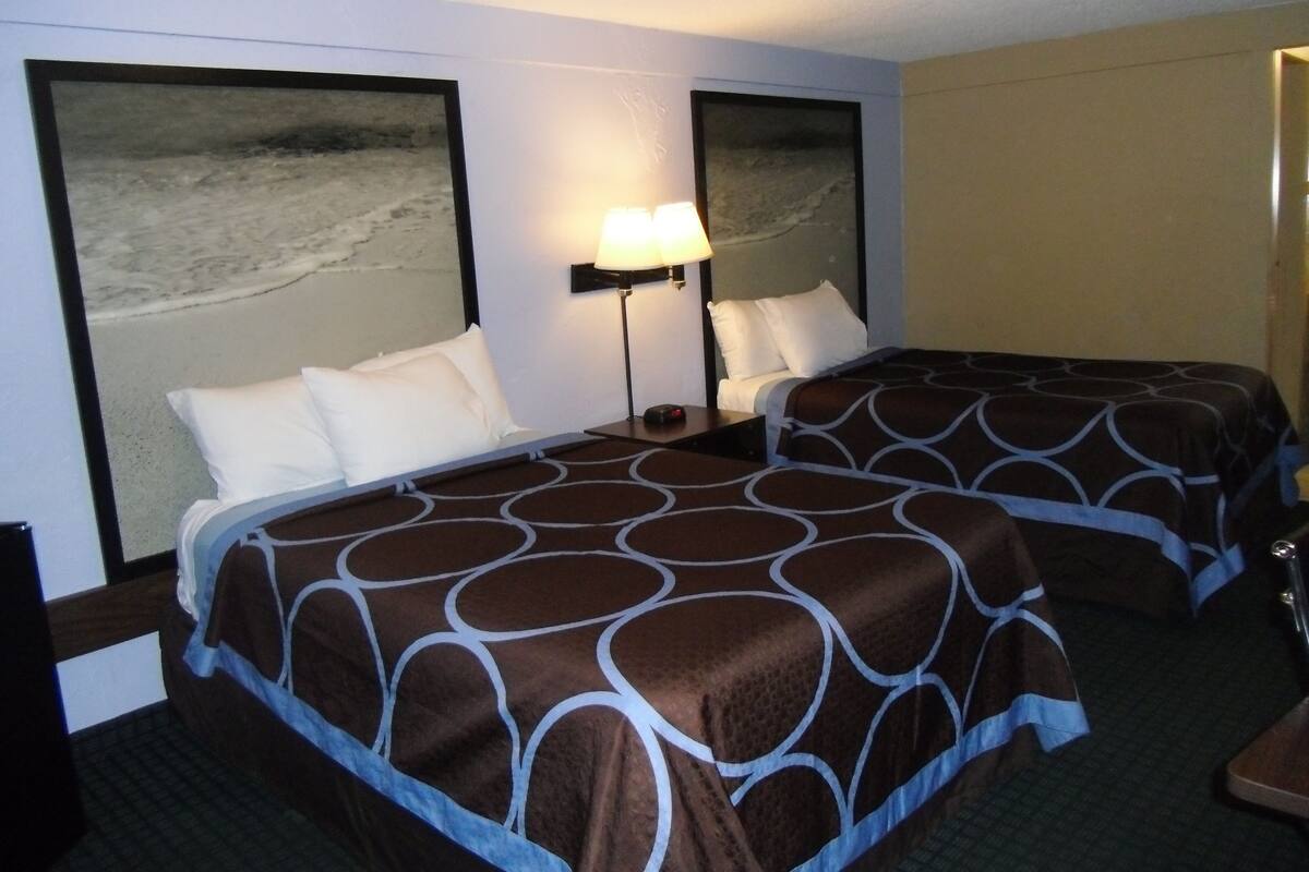 A hotel room with two beds, a nightstand, a lamp, and a large mirror.