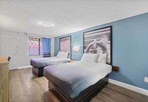 A bedroom with two beds, a window with curtains, a door, and a wall-mounted lamp.