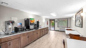 A modern kitchen area with a coffee machine, microwave, and refrigerator. There are wooden cabinets and a tiled floor. - Super 8 by Wyndham Lantana West Palm Beach (Lantana)