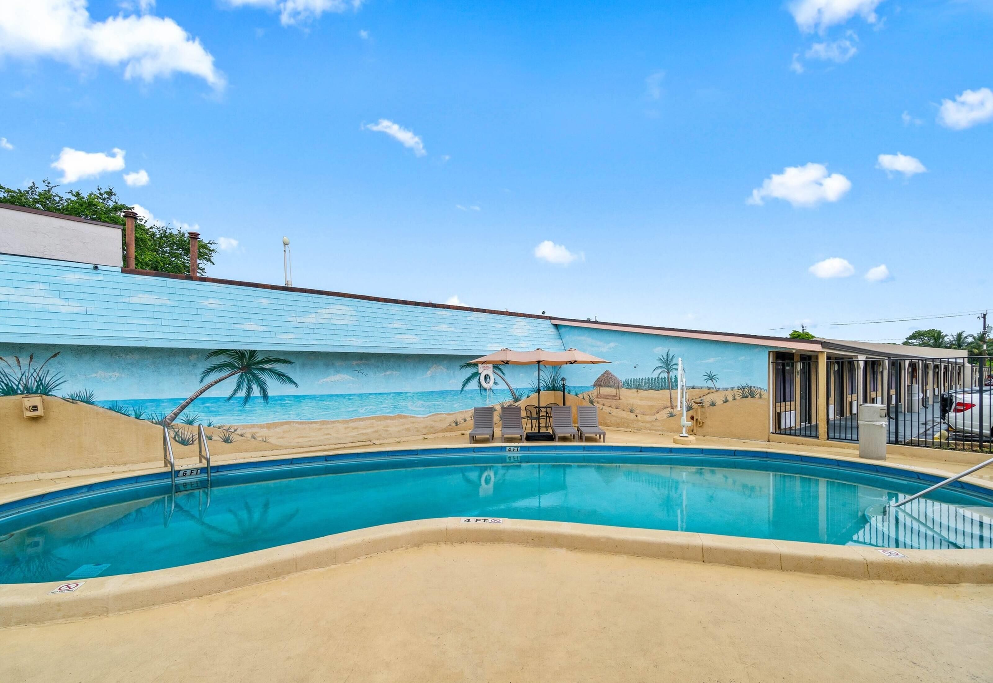 A swimming pool with a mural of a beach scene, a lifeguard chair, and a few lounge chairs.