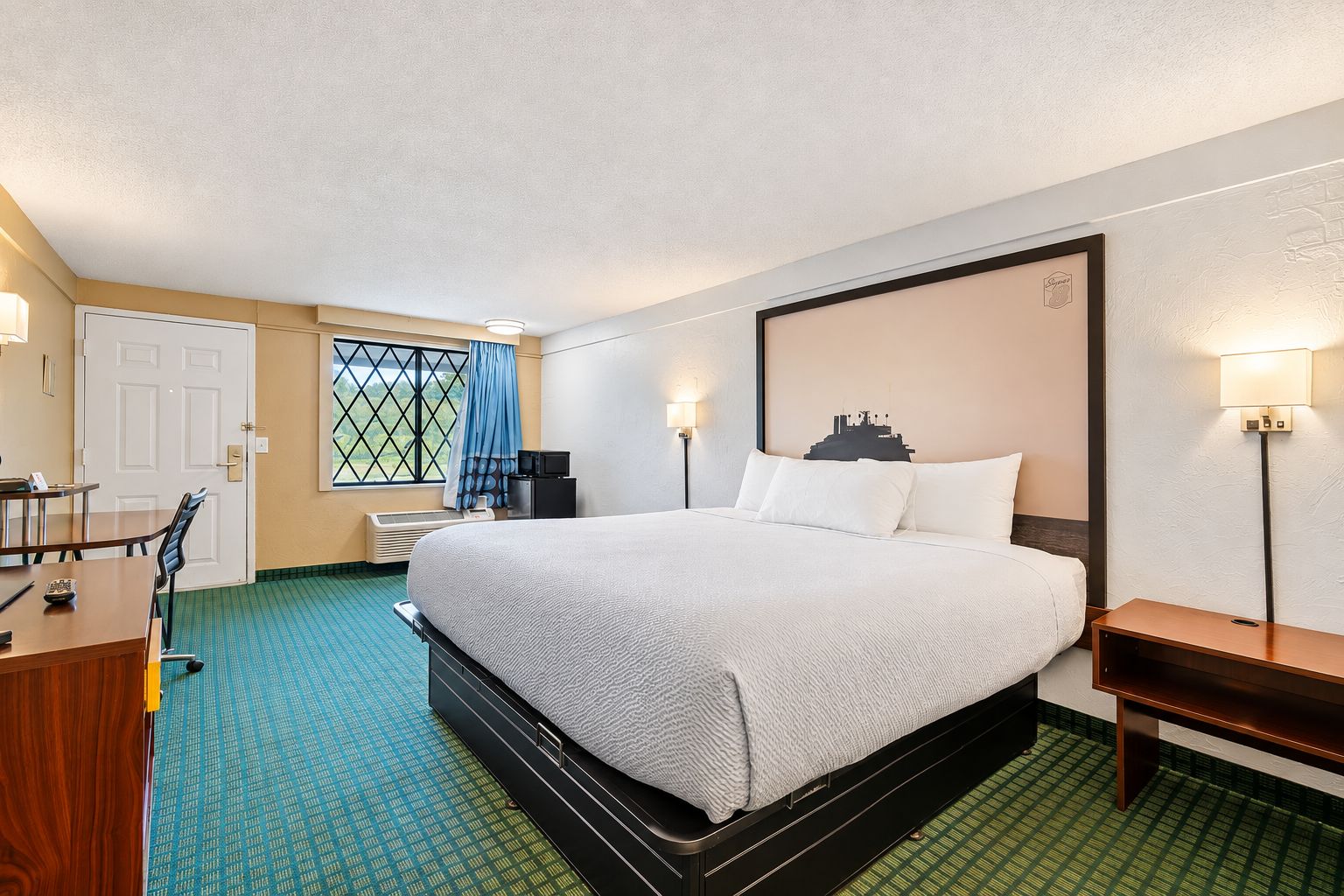 A hotel room with a bed, a desk, a chair, a TV, and a window with curtains.