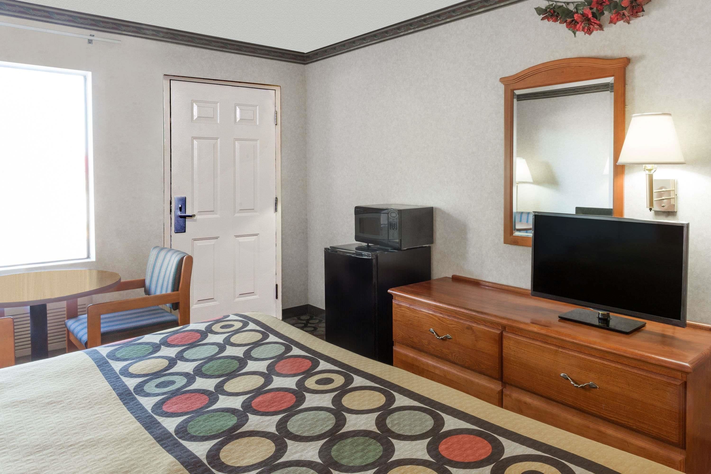 Una habitación de hotel con cama, escritorio y silla, televisor, refrigerador y cómoda.