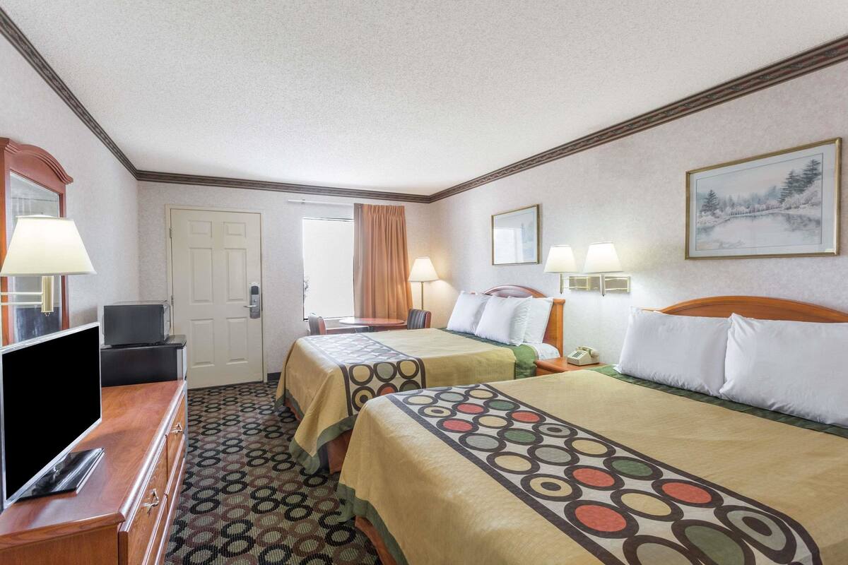 Quarto de hotel com duas camas, televisão, escrivaninha e porta.