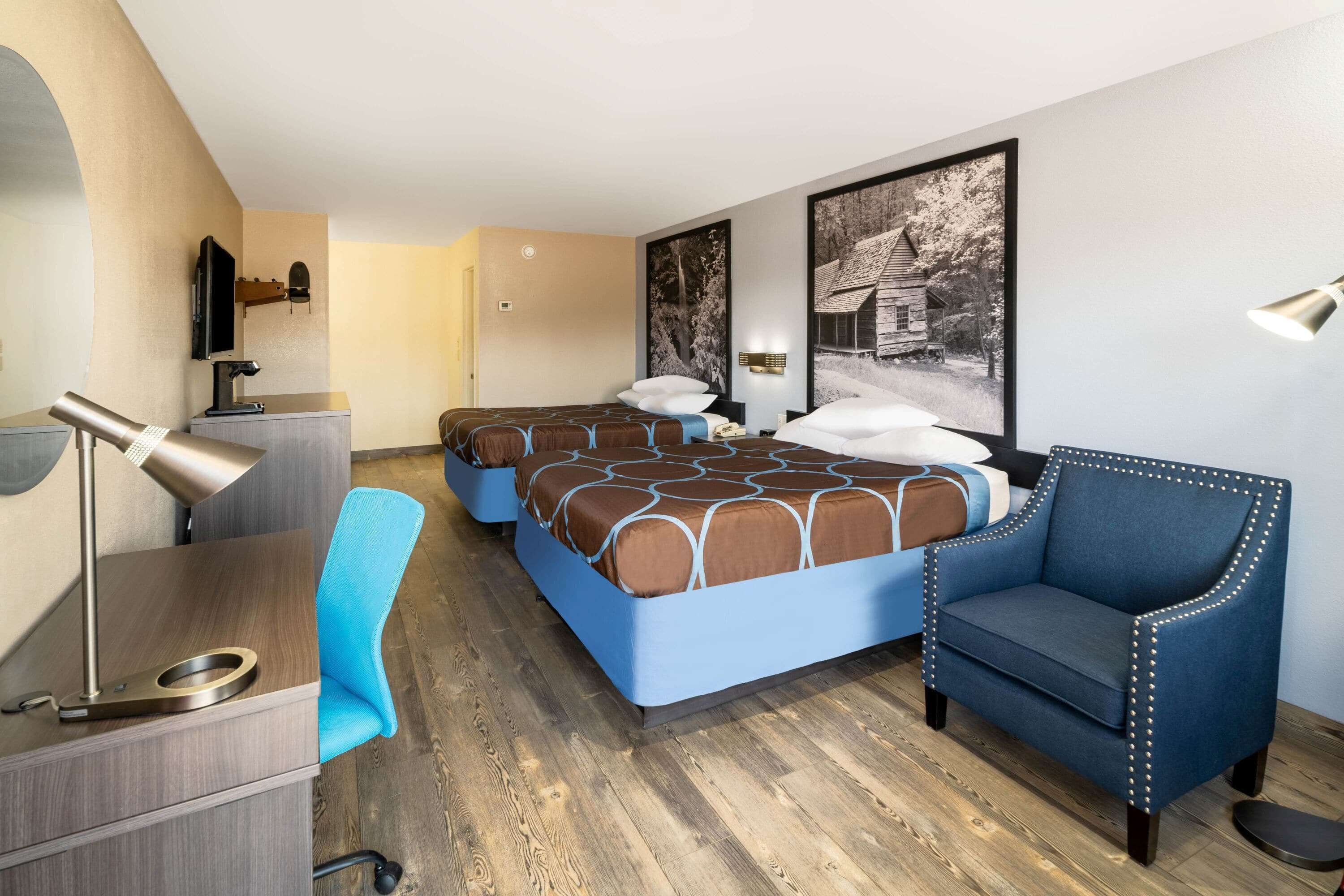 Habitación de hotel con una cama grande, un escritorio, una silla, un televisor y dos cuadros en la pared.