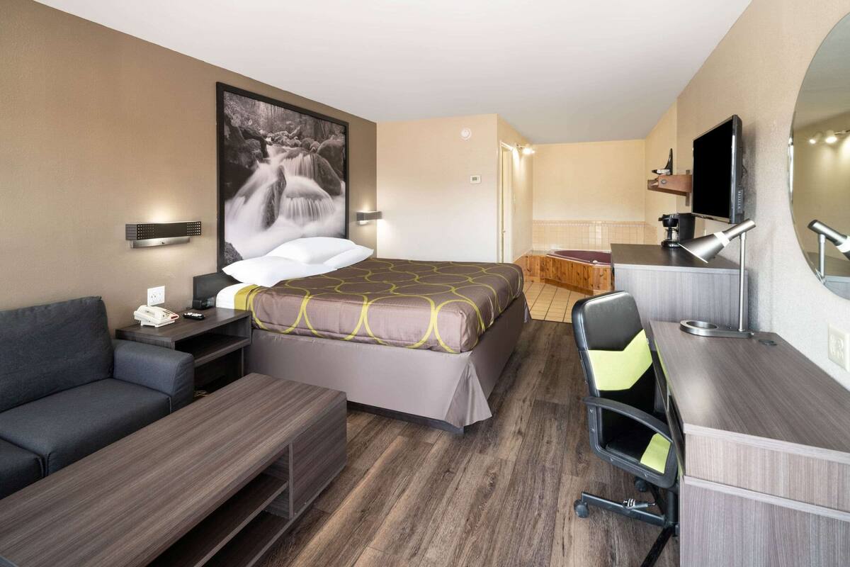 A hotel room with a bed, a desk, a chair, a sofa, a TV, and a bathroom.