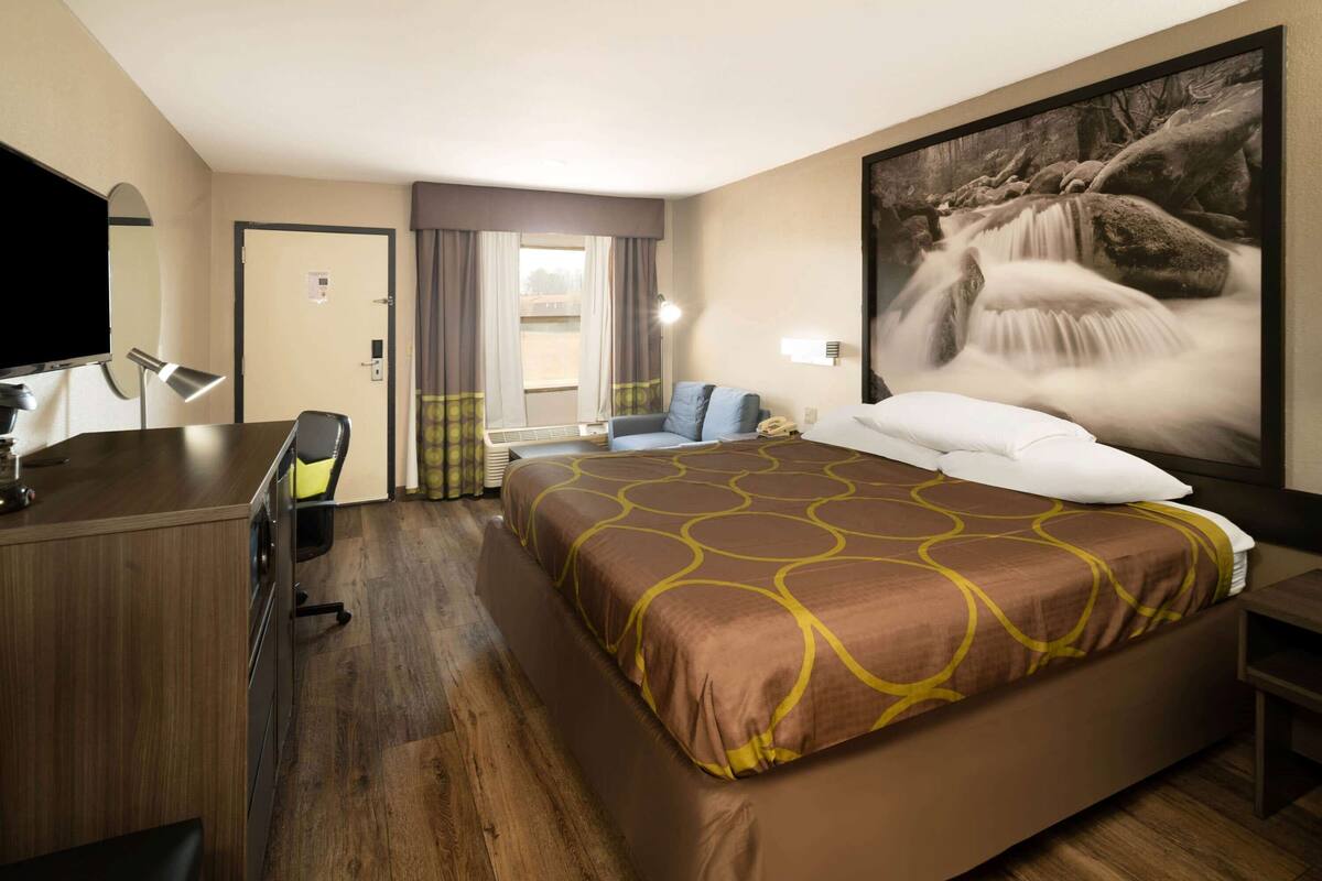 A hotel room with a large bed, a desk with a chair, a TV, and a large window with curtains.