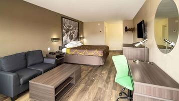 A hotel room with a bed, a sofa, a desk, a chair, a TV, and a large mirror.