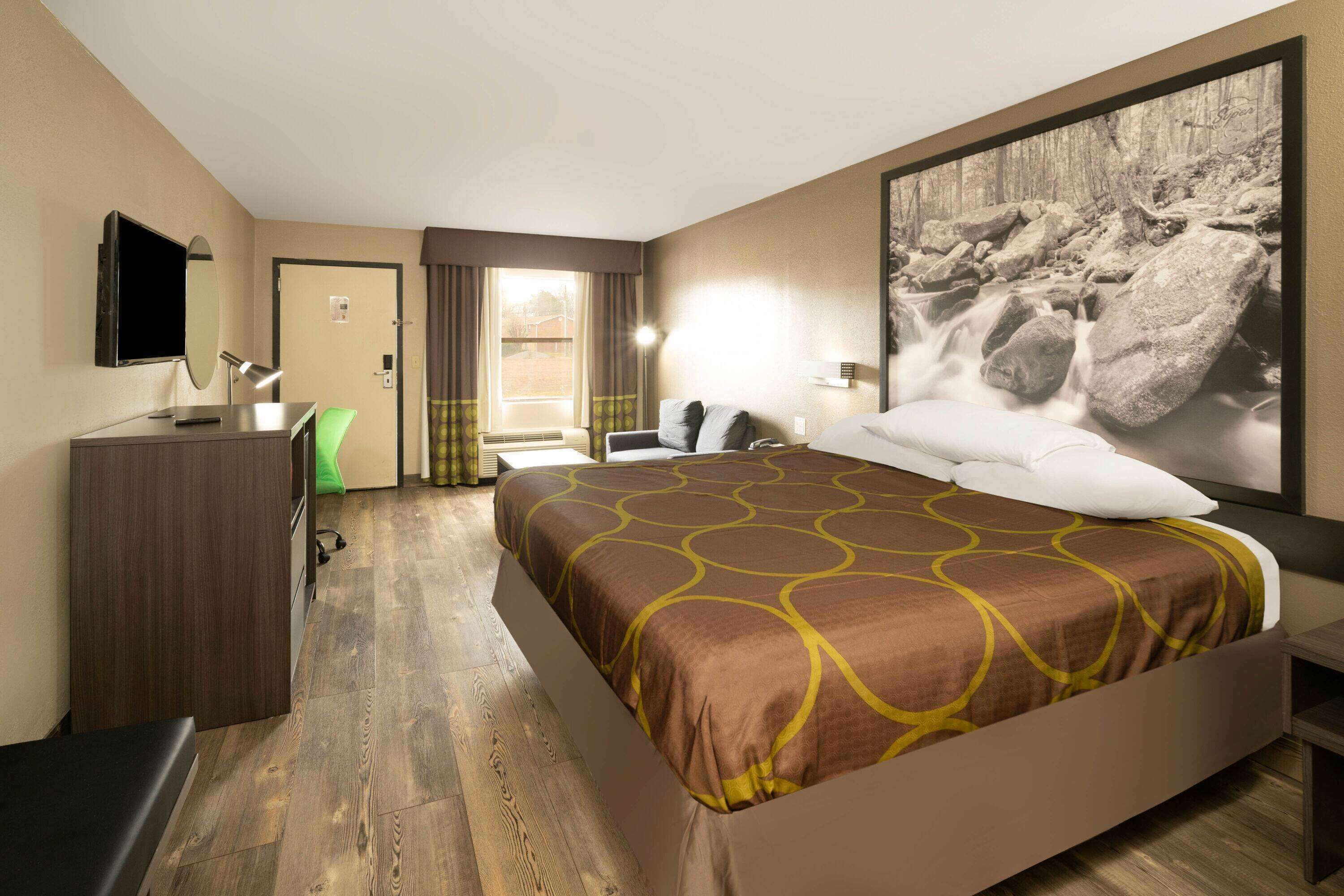Una habitación de hotel con cama, escritorio, silla, televisión y ventana grande.
