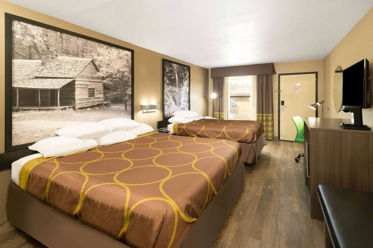 A hotel room with two beds, a desk, a television, and large framed pictures on the wall.