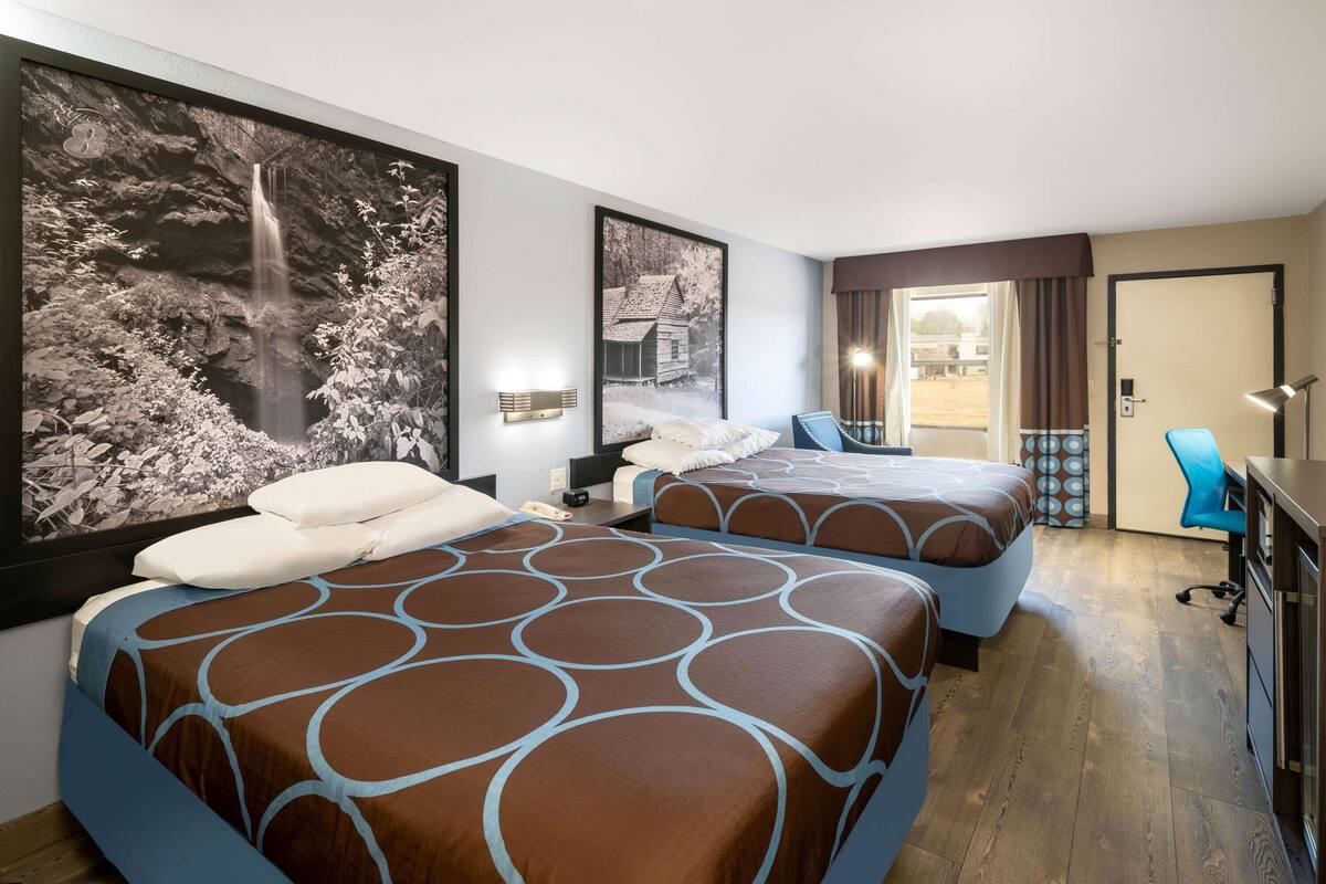 A hotel room with two beds, a desk, a chair, and a large window.