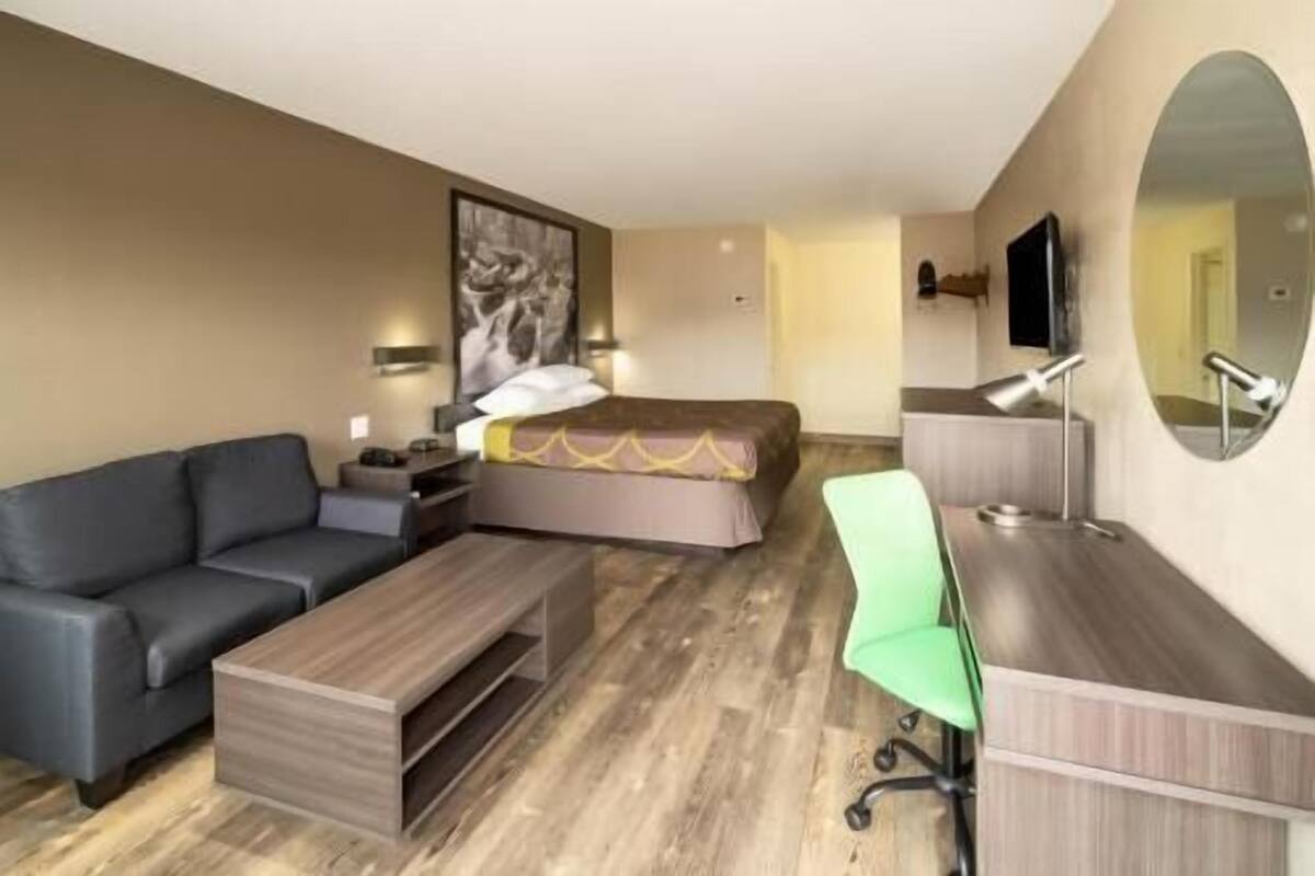 A hotel room with a bed, a sofa, a desk, a chair, a TV, and a mirror.