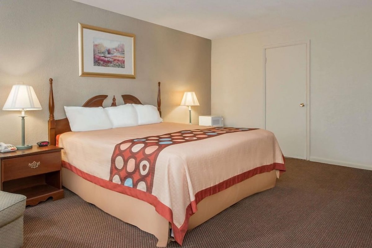 A hotel room with a bed, two bedside lamps, a nightstand, a framed picture on the wall, and a door.
