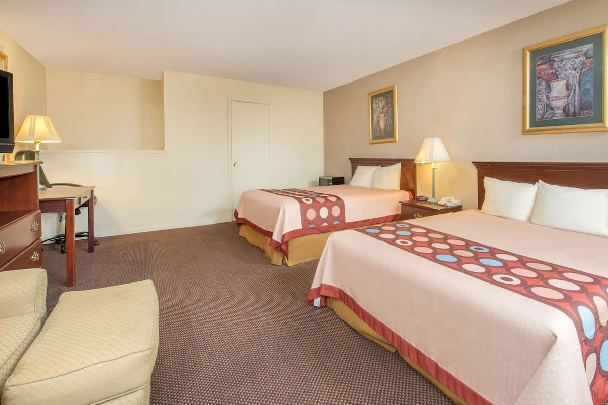 Quarto de hotel com duas camas, uma escrivaninha, uma cadeira e uma televisão.