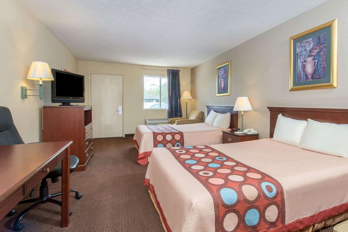 Quarto de hotel com duas camas, uma escrivaninha, televisão e janela com cortinas.