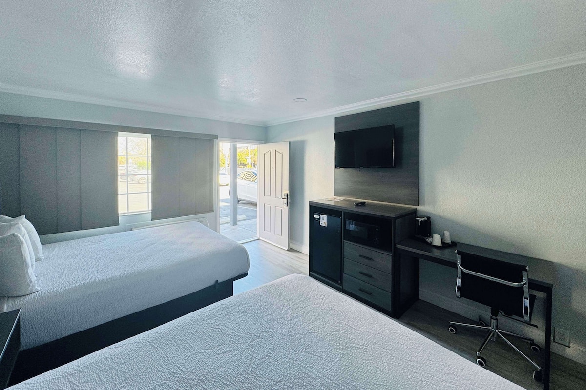 Une chambre d’hôtel avec deux lits, un téléviseur à écran plat fixé au mur, un bureau avec des tiroirs et une petite chaise de bureau.