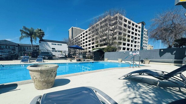 A swimming pool with lounge chairs, a stone planter, and a multi-story building in the background. - SureStay by Best Western Fresno Central (Fresno)
