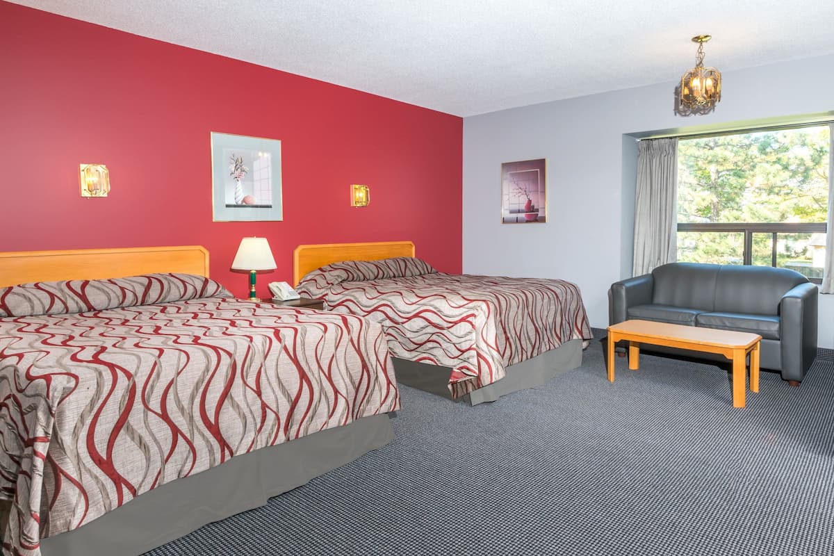 A hotel room with a large bed, a sofa, a small table, and a window with a view of trees.