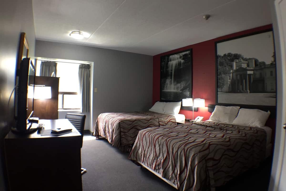 A hotel room with two beds, a desk with a lamp, a TV, and a large window.