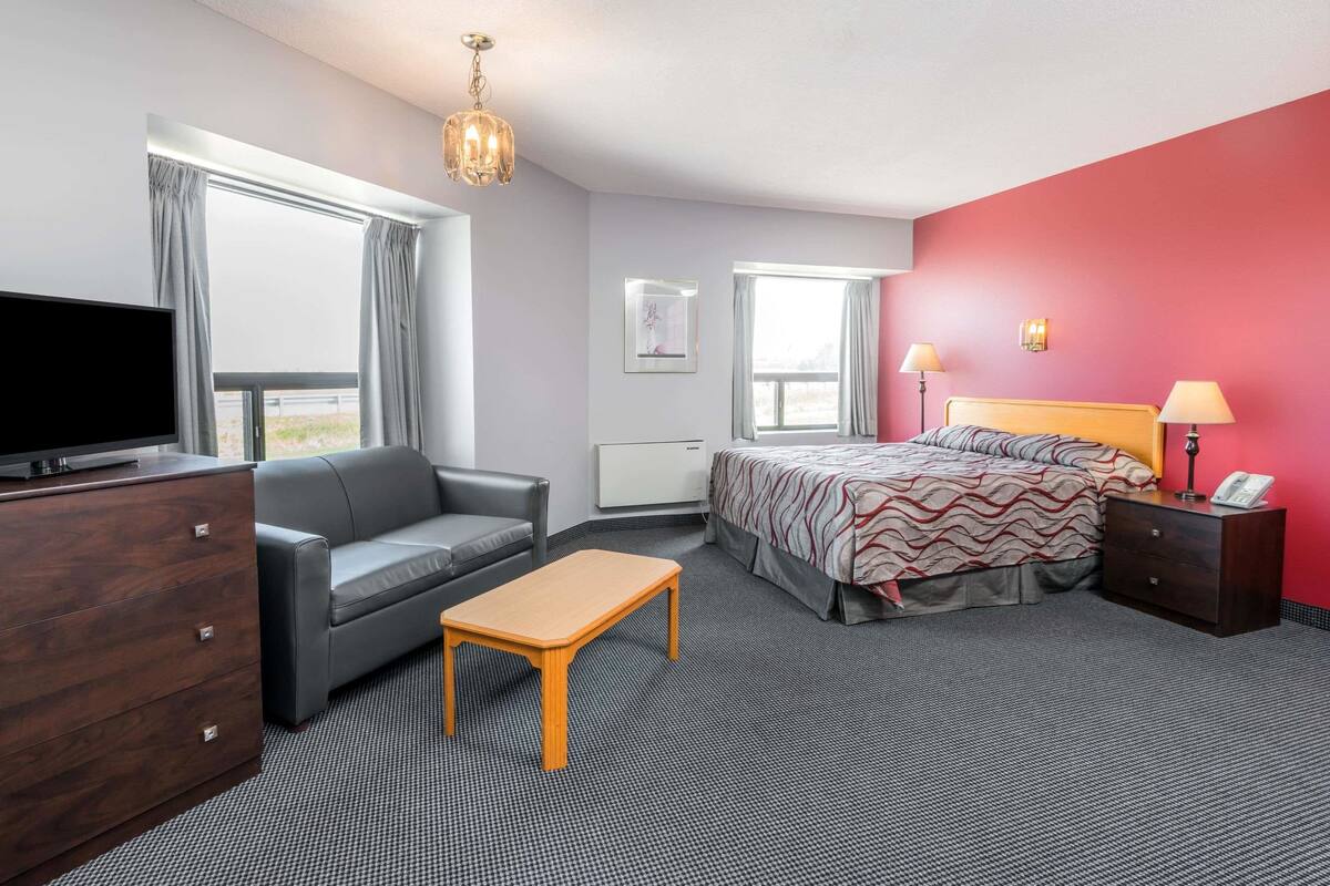 A hotel room with a bed, a desk, a sofa, a TV, and a window with curtains.