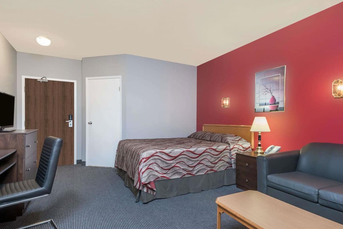 A hotel room with a bed, a desk, a chair, a sofa, a lamp, and a painting on the wall.