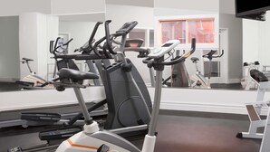 A gym with various exercise machines, a large mirror, and a window with orange curtains.