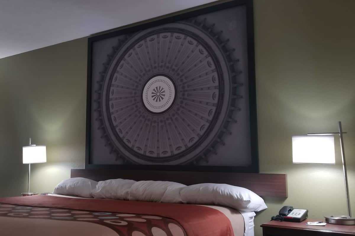 Een hotelkamer met een grote ronde wanddecoratie, een bed met een gestreept sprei, twee bedlampen en een nachtkastje met een telefoon en een klein tafeltje.