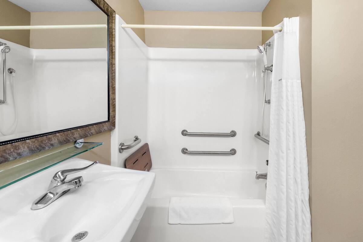Een moderne badkamer met een glazen plank, een witte wastafel, een bad en een douche.