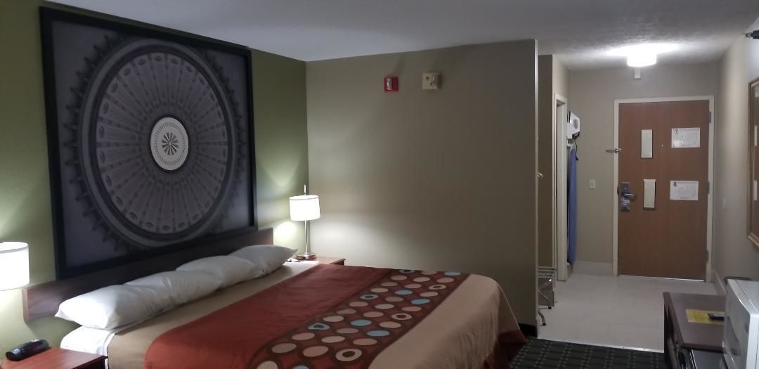 Habitació d'hotel amb un llit gran, un capçal amb disseny circular, una tauleta de nit amb una làmpada i una porta amb mirall i notes.