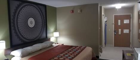 A hotel room with a large bed, a headboard with a circular design, a bedside table with a lamp, and a door with a mirror and notes.