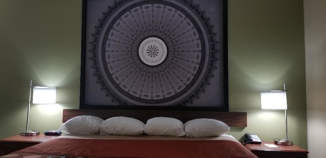 Een hotelkamer met een grote ronde wanddecoratie, een bed met witte kussens en twee bedlampjes.