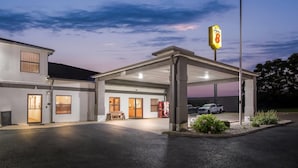 Un motel con área de estacionamiento techada, edificio de una sola planta y entrada visible.