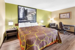 Habitación de hotel con una cama grande, un escritorio, una silla, una lámpara y un cuadro en la pared.