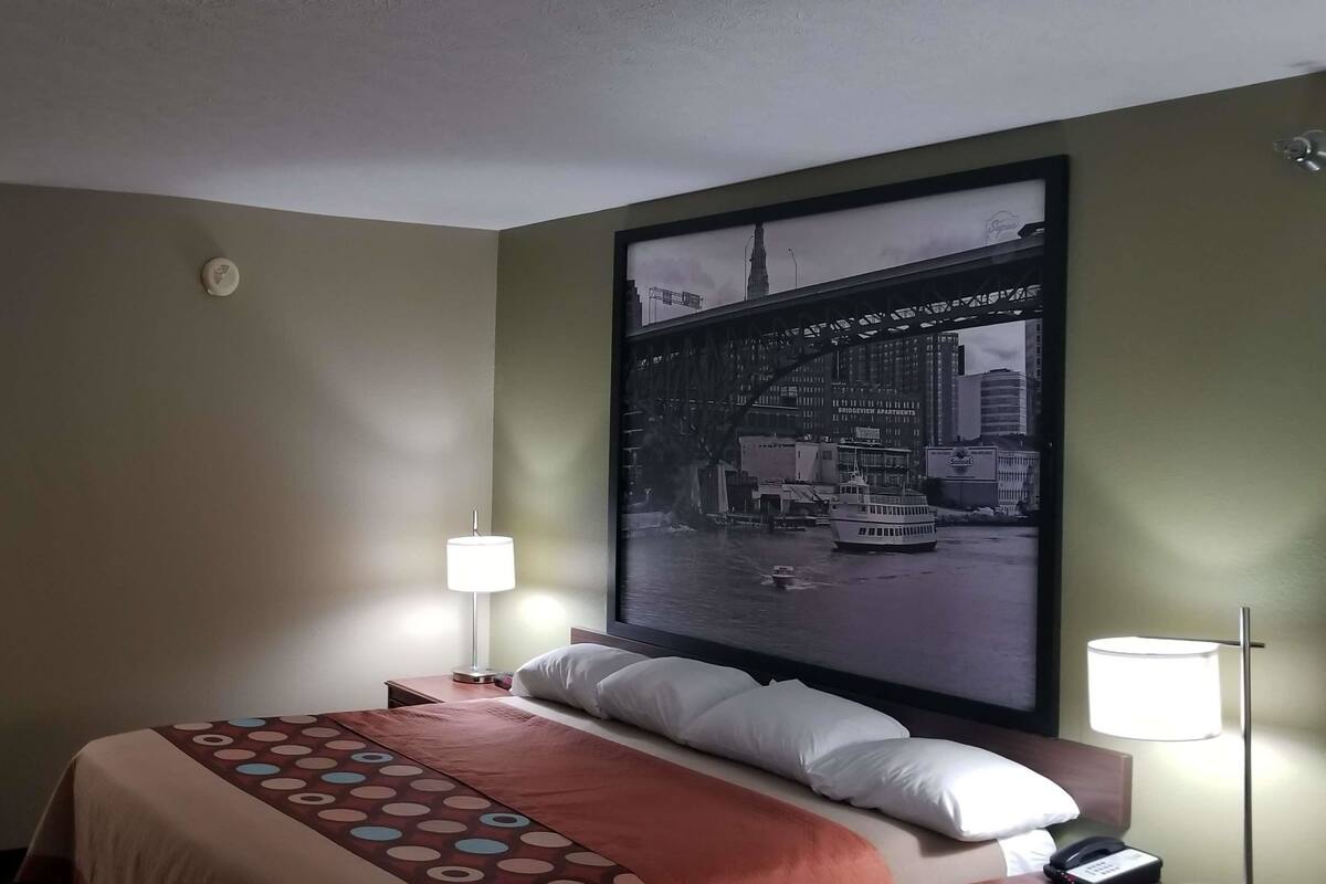 Hotelkamer met een bed, twee bedlampen, een groot stadsgezichtposter aan de muur en een tafeltje met een telefoon.
