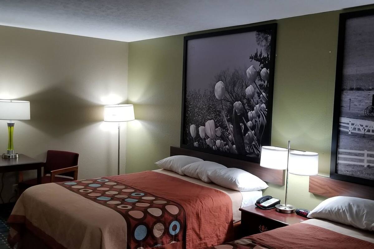 Hotelkamer met een bed, twee nachtkastjes met lampen, een stoel en een groot beeld in een lijst aan de muur.