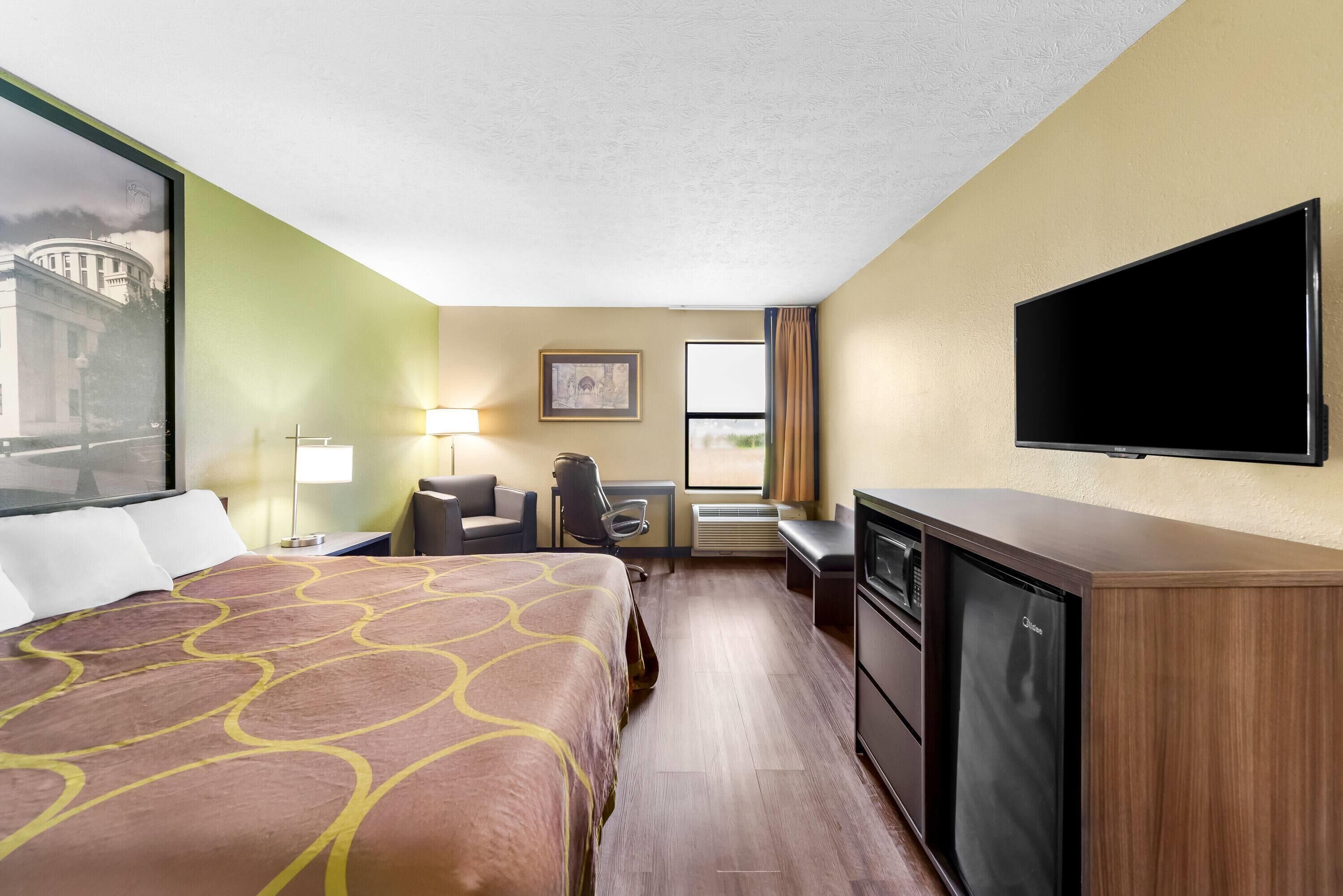 A hotel room with a bed, desk, chair, television, and a window with curtains.