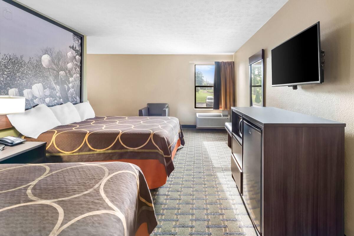 Een hotelkamer met twee bedden, een flatscreen televisie, een bureau met lamp, een dressoir en een groot raam met uitzicht op de omgeving.