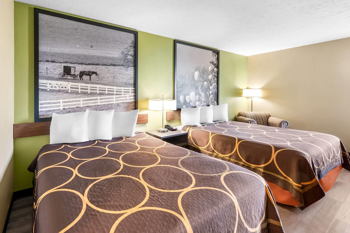 Hotelkamer met twee bedden, elk voorzien van een beddekleed met dessin, een groot, ingelijst kunstwerk aan de muur en een nachtkastje met lamp.