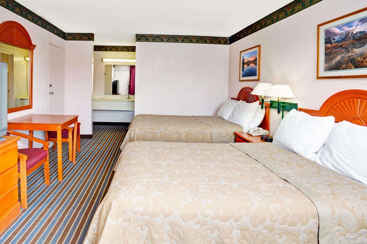 Une chambre d’hôtel équipée d’une télévision, d’un bureau, de deux lits, d’une salle de bain et ornée d’un tableau au mur.
