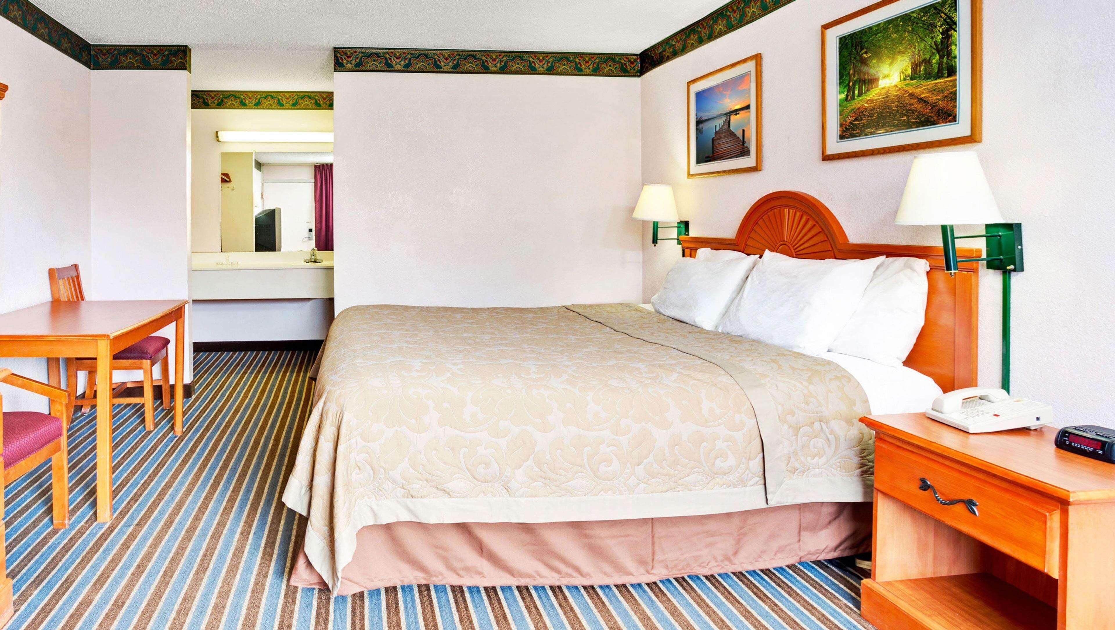 Une chambre d’hôtel comprenant un lit, une table de chevet, une lampe, une chaise et un bureau avec un miroir.