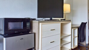 Een kleine hotelkamer met kitchenette, een flatscreen televisie, bureau met lamp en een stoel.