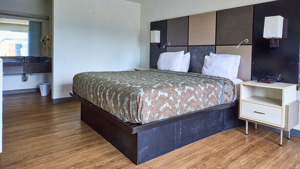 Een hotelkamer met een bed, nachtkastje en een klein bureau met lamp.