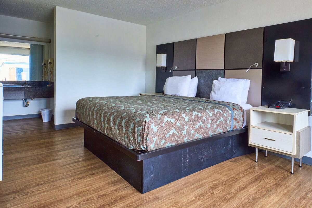 Ein Hotelzimmer mit Bett, Nachttisch und einem kleinen Schreibtisch mit Lampe.
