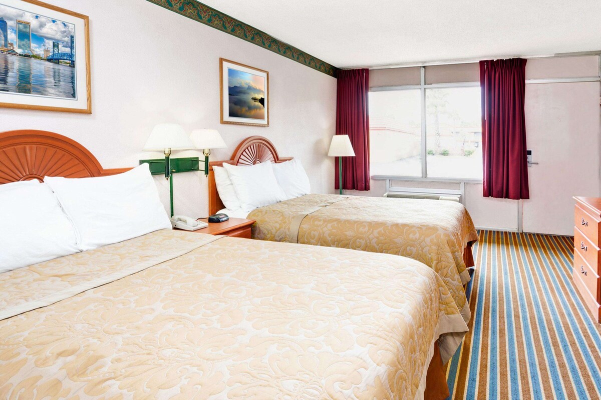 Une chambre d’hôtel avec deux lits, un bureau, une télévision et une fenêtre avec des rideaux.