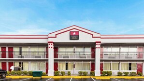 Een hotel met twee verdiepingen, een gevel in rood en wit, een opvallend bord met daarop 'Magnuson Hotel Jacksonville Downtown' en een parkeerplaats met een groene afvalcontainer.