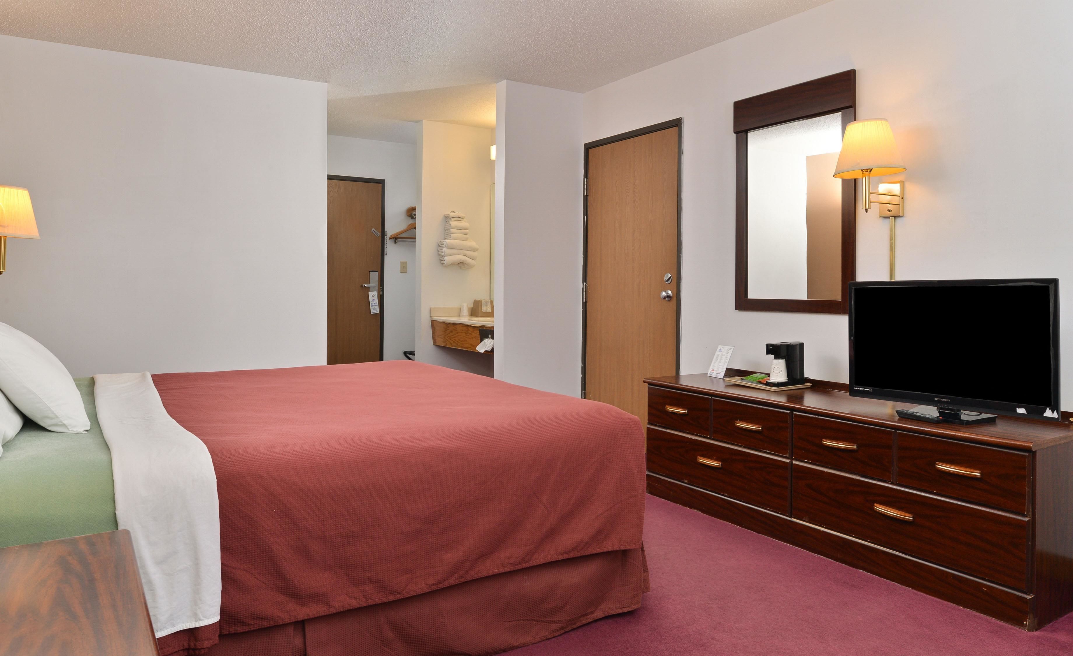 A hotel room with a bed, a dresser, a television, and a mirror.