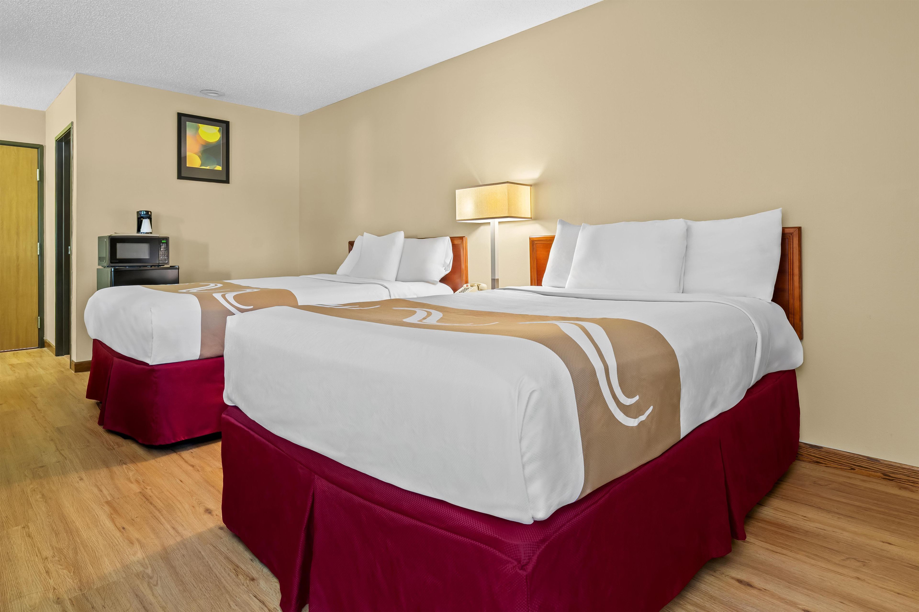 A hotel room with two beds, a desk with a computer, a lamp, and a painting on the wall.